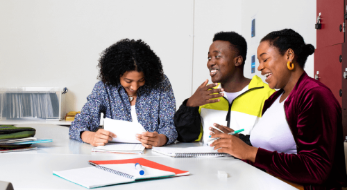Young people of colour sit at a table inside and talk and laugh
