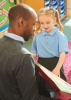 Black teacher reads a book to a white schoolchild in a classroom