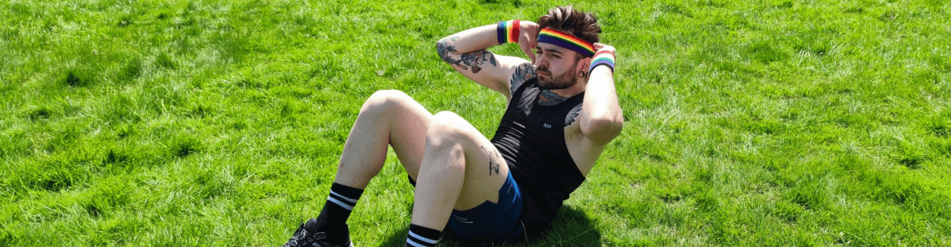 A white person doing sit ups on a field, wearing a rainbow headband